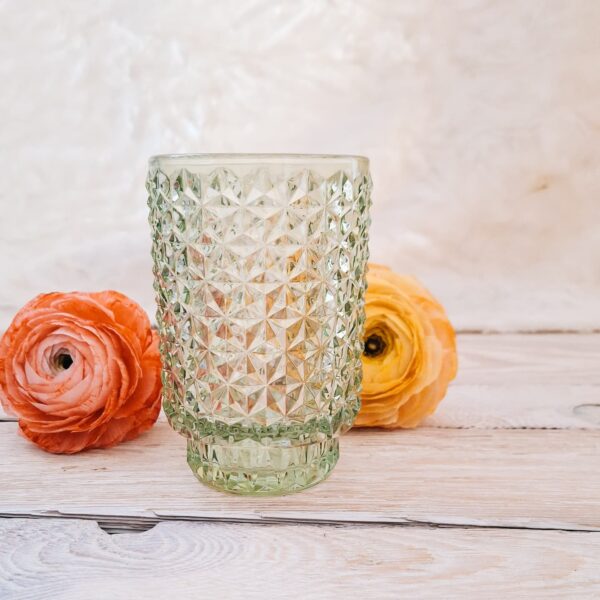 zielony, szklany wazon i lampion w jednym w otoczeniu zółtego i pomarańczowego jaskra z papieru